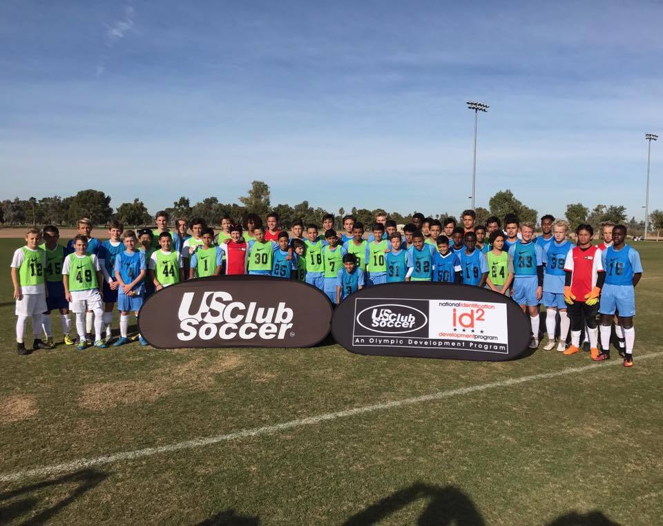 Youth soccer players posing with US Club Soccer and id2 Development Program pop-up banners on an outdoor field