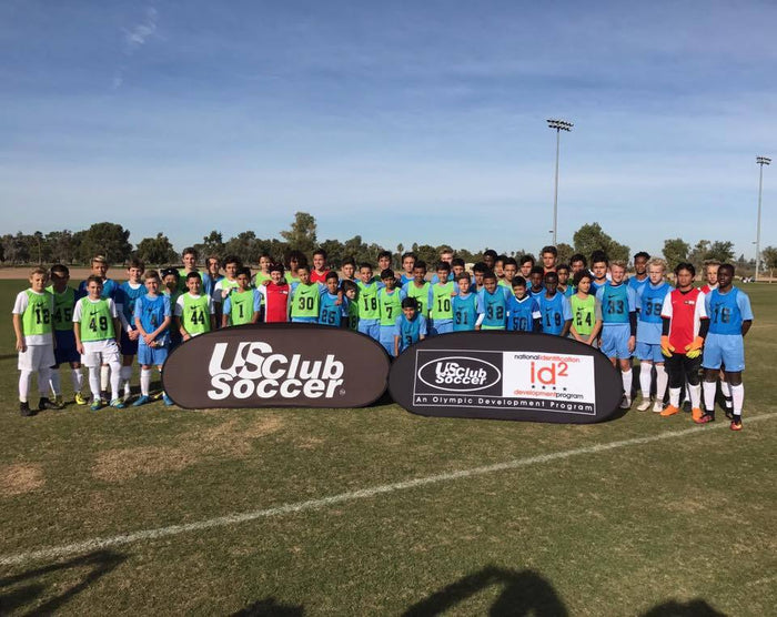 Youth soccer players posing with US Club Soccer and id2 Development Program pop-up banners on an outdoor field