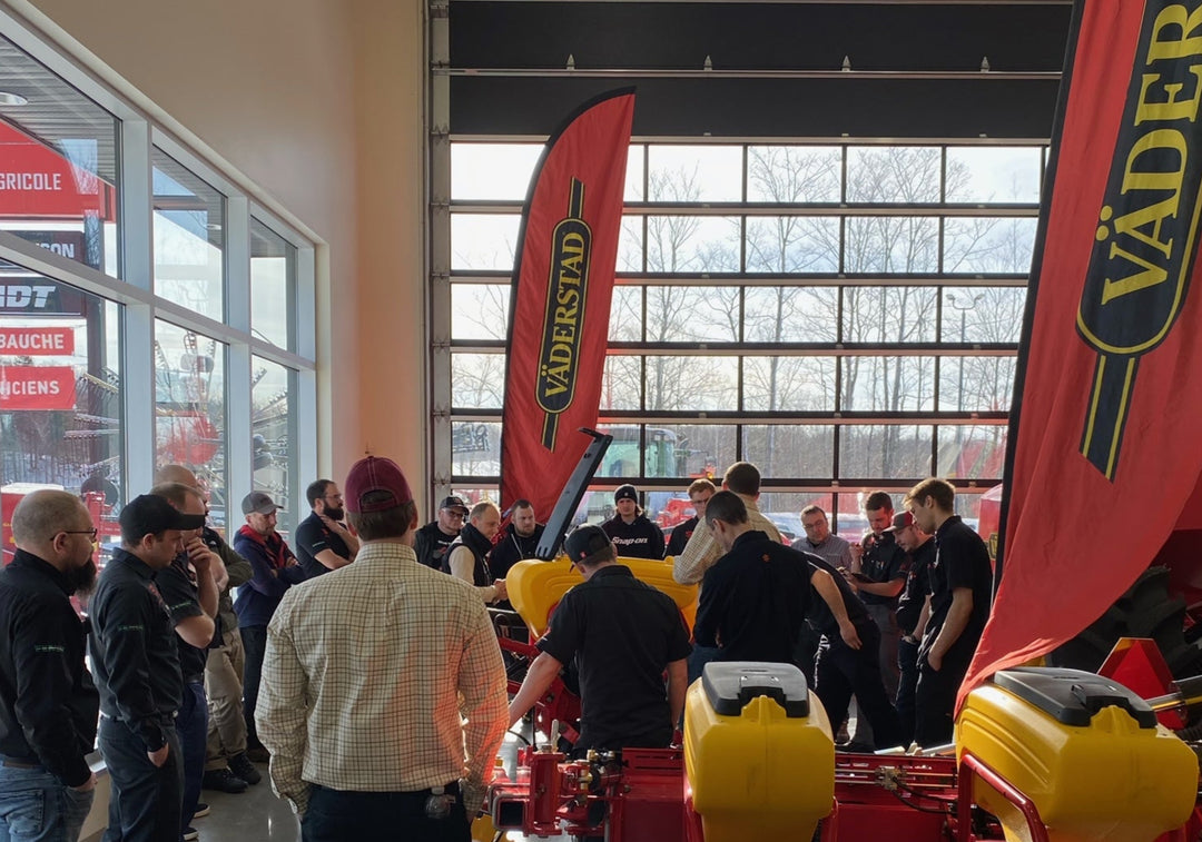 Indoor agricultural equipment demonstration with group of people and red Vaderstad feather flags.