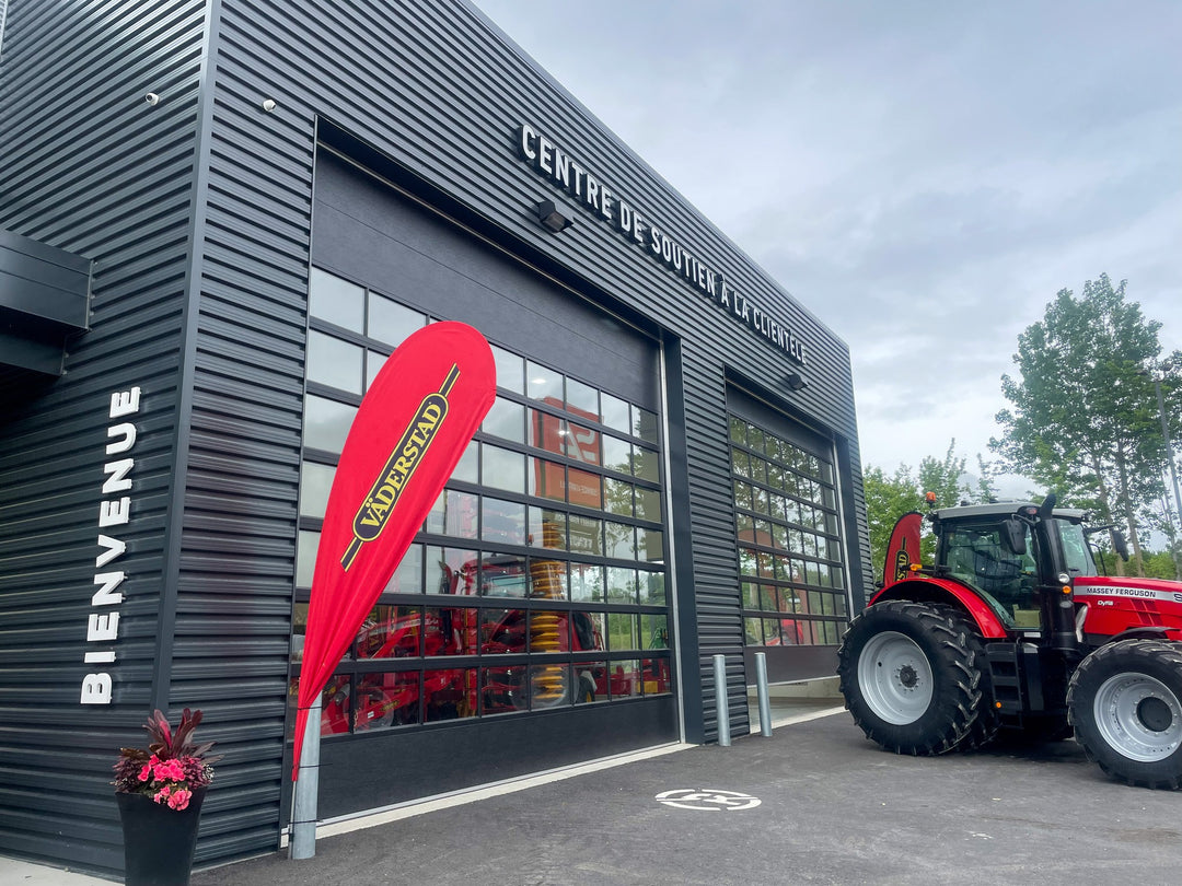 Red teardrop flag with Väderstad logo displayed outside a black industrial building labeled "Centre de Soutien à la Clientèle" with a red Massey Ferguson tractor parked nearby