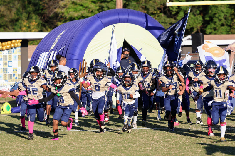 Football team running onto the field with a large inflatable arch in the background