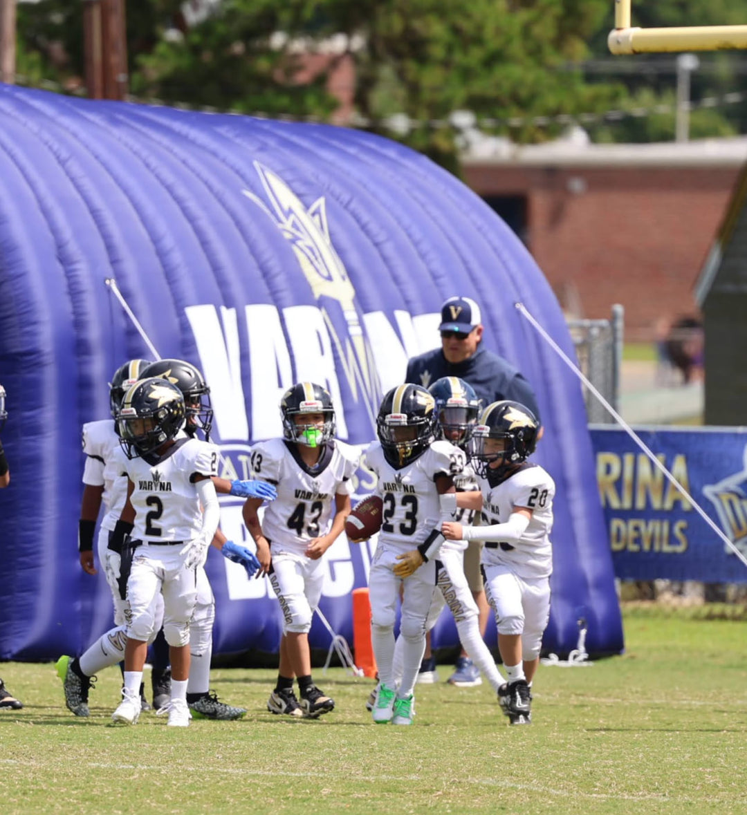 Young Varina Blue Devils football players in white uniforms standing outside inflatable tunnel
