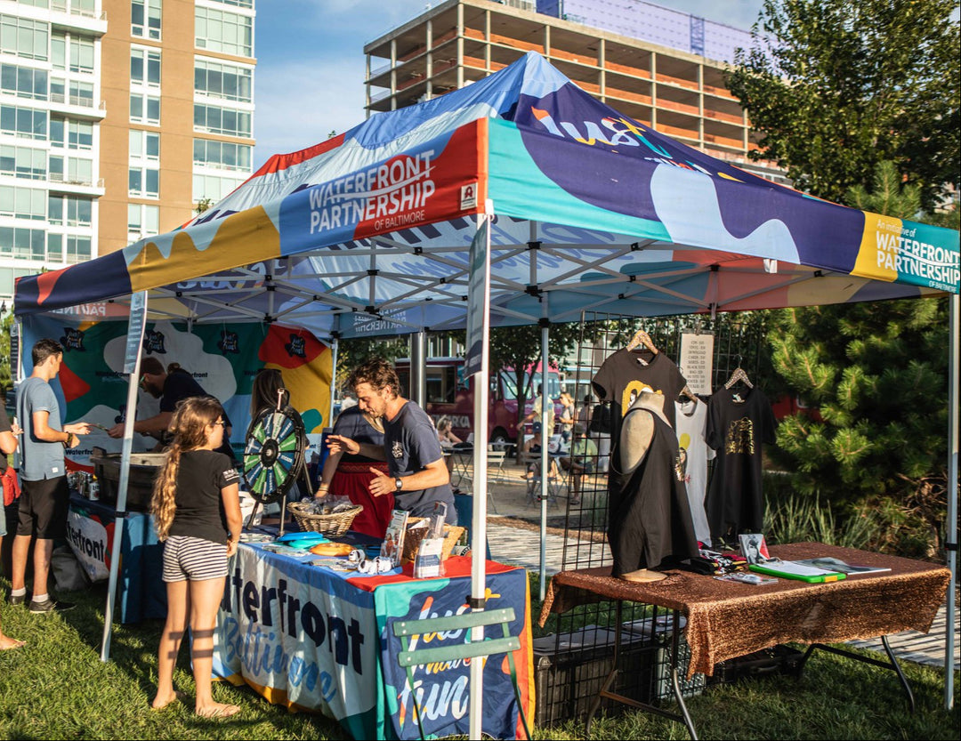 Waterfront Partnership of Baltimore colorful canopy tent at outdoor city event with attendees and merchandise display