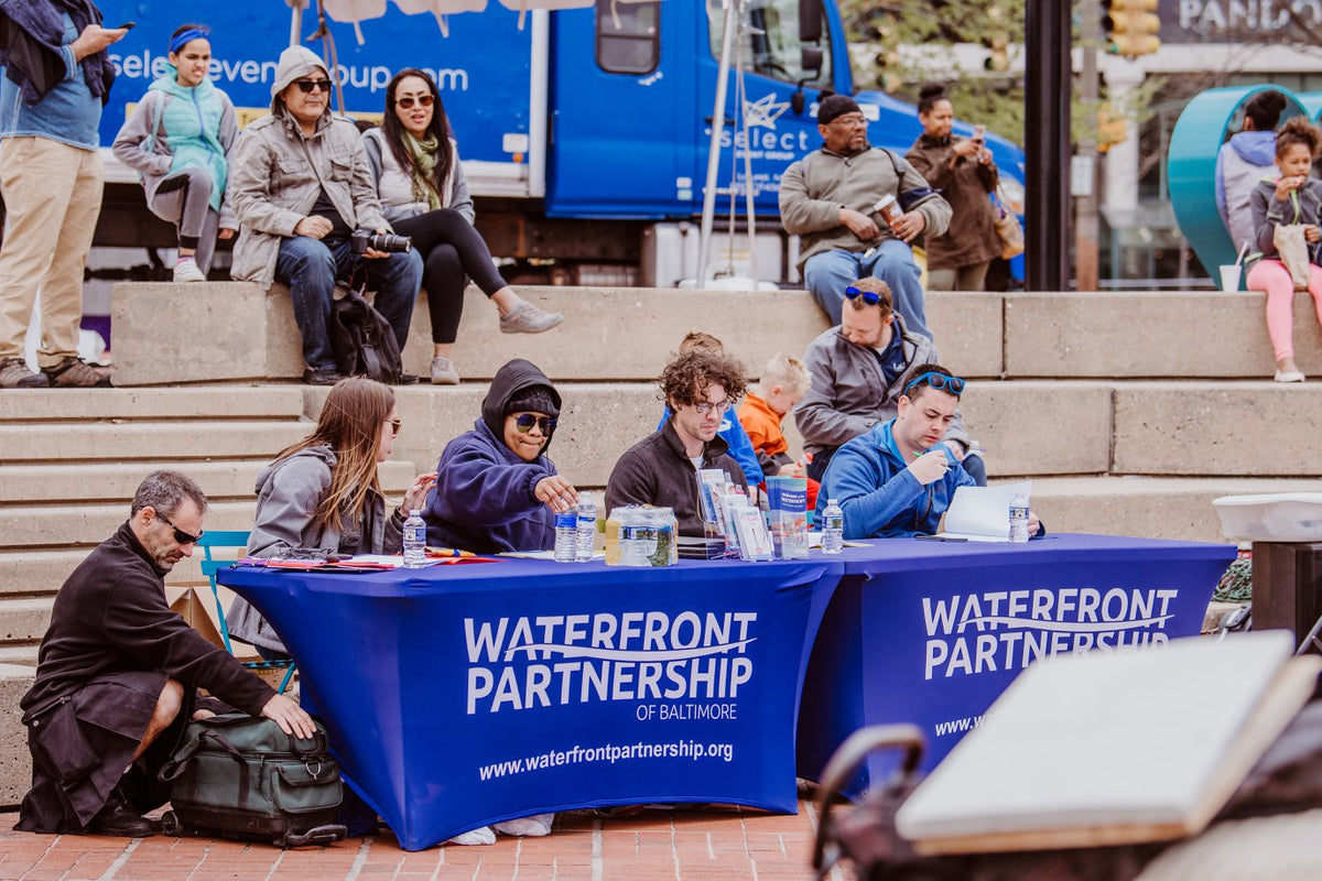People sitting at a table with 'Waterfront Partnership of Baltimore' branding in an outdoor setting.