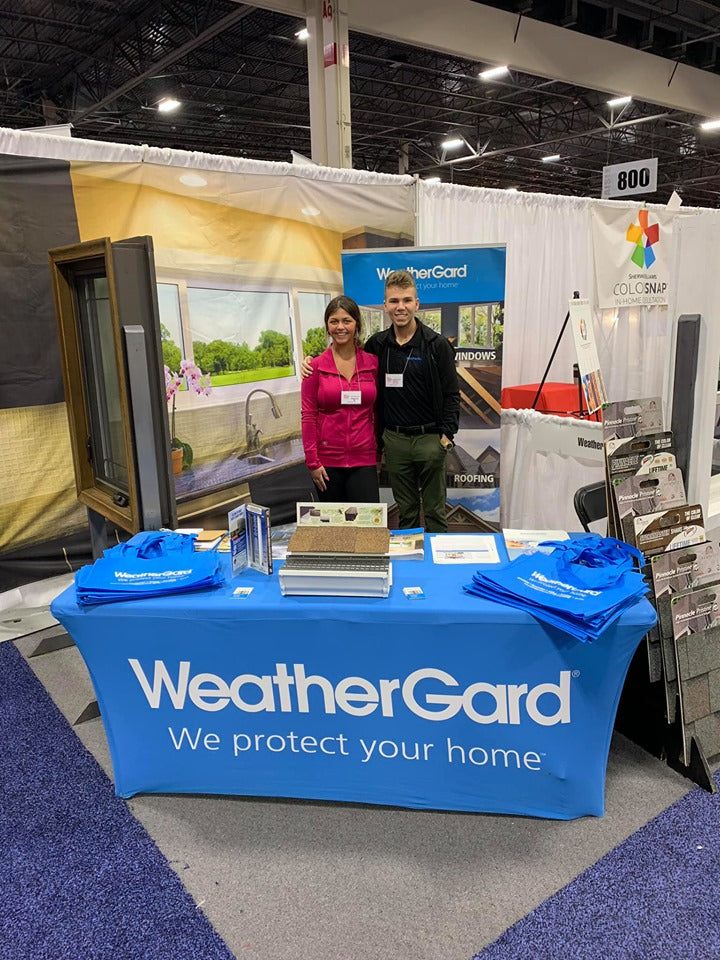 Two people standing behind a WeatherGard booth at an event with promotional materials.